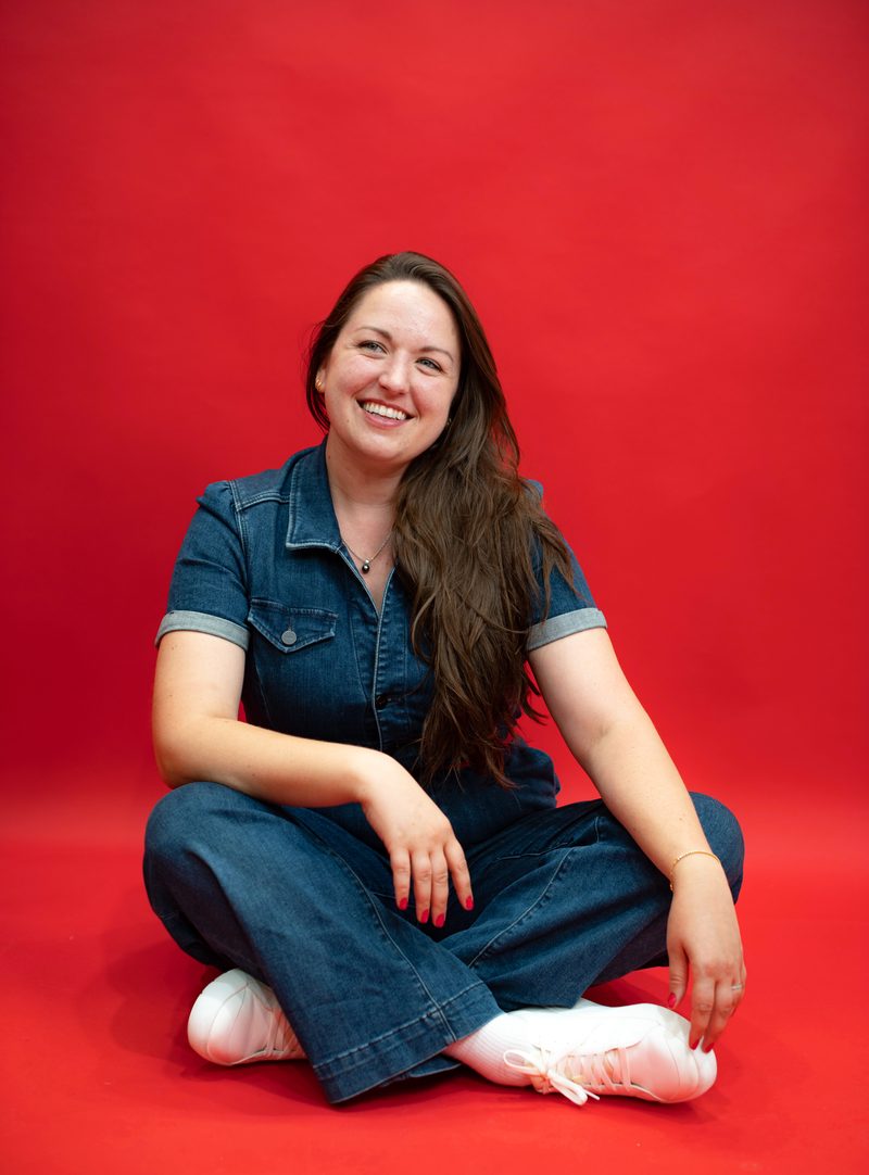 Jessica Tenuta sitting cross-legged against a red studio backdrop